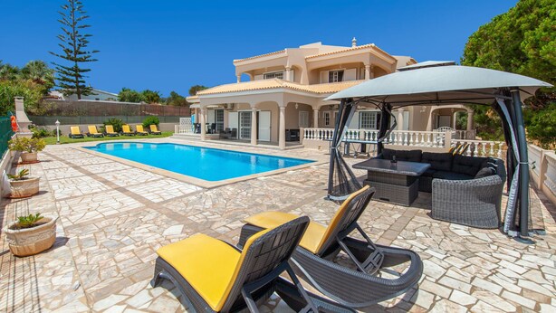 Un área junto a la piscina con sillones de descanso, una zona de estar techada y una piscina.