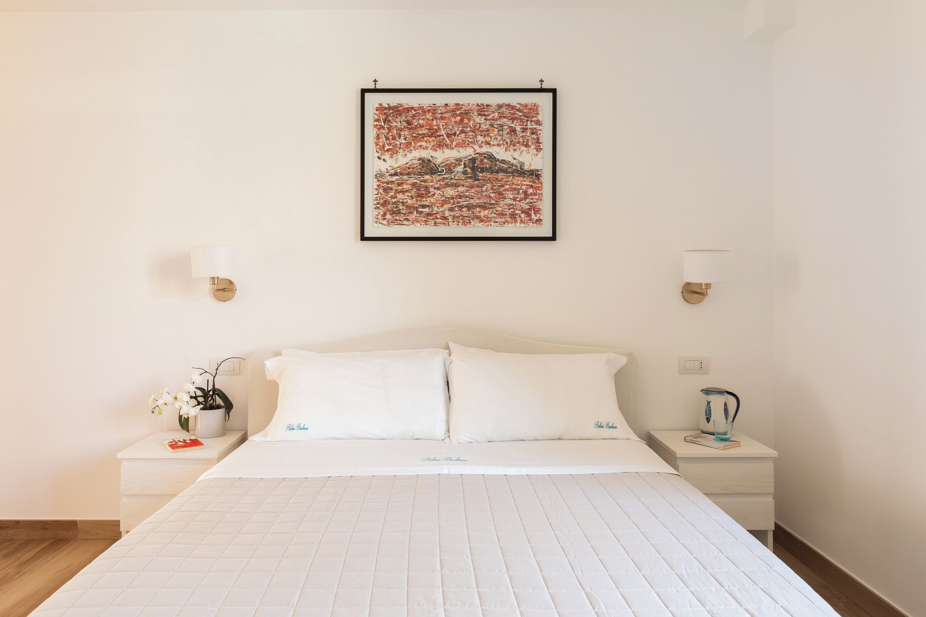 Een netjes ingerichte hotelkamer met een groot bed, twee nachtkastjes, een ingelijste afbeelding aan de muur en een potplant op een van de nachtkastjes.