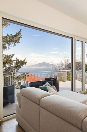 A modern living room with a large sliding glass door leading to a balcony with a scenic view of the sea and mountains. - YourHome - Relais Barbara (Sorrento)