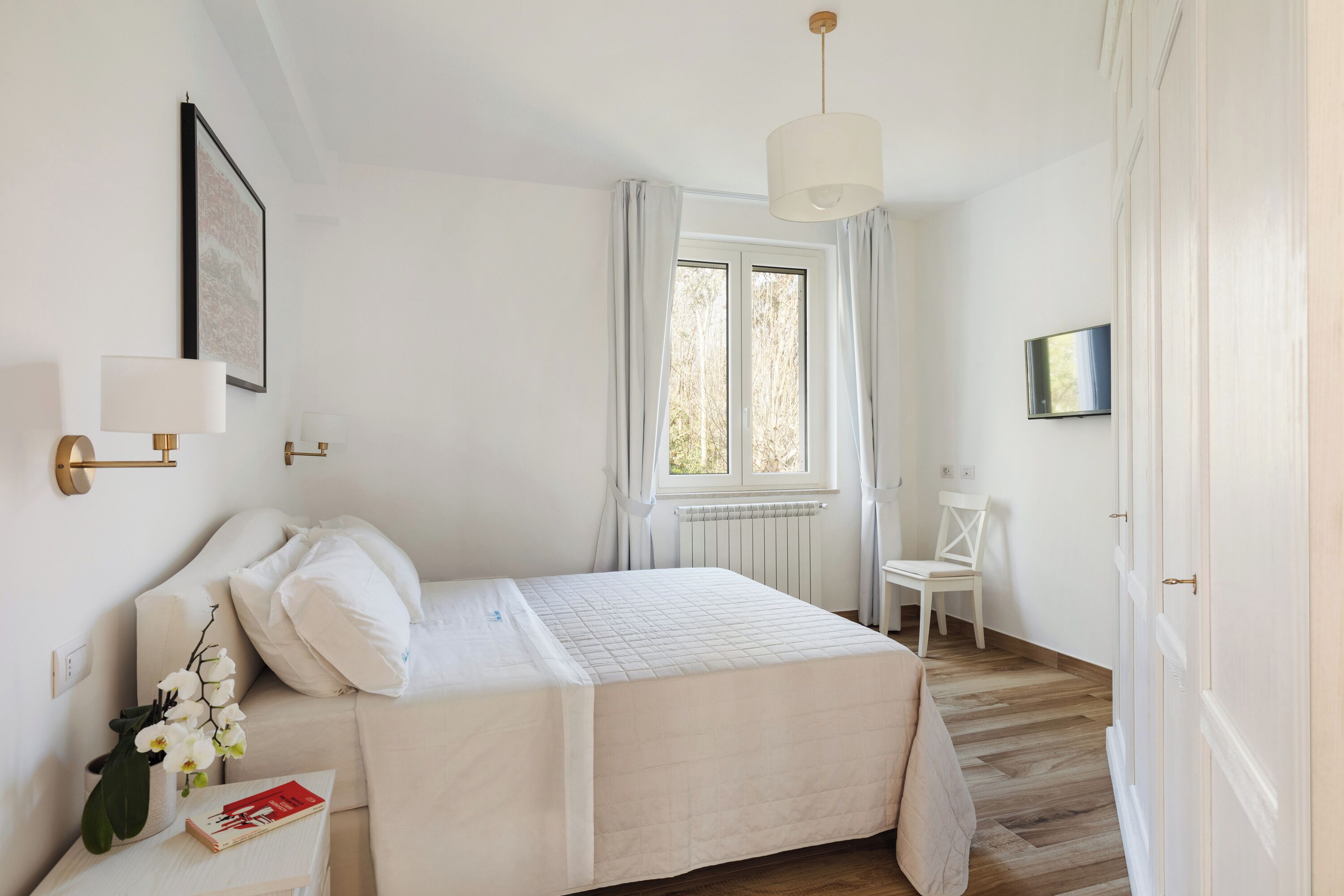 A bedroom with a bed, a nightstand, a chair, a window, and a radiator.