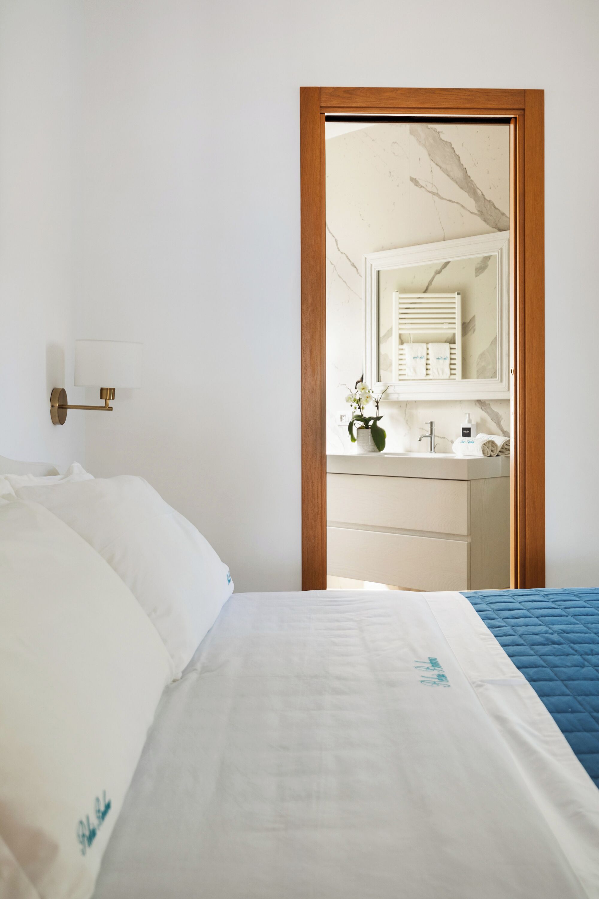 A bedroom with a bed, a nightstand, a mirror, and a bathroom visible through an open door.