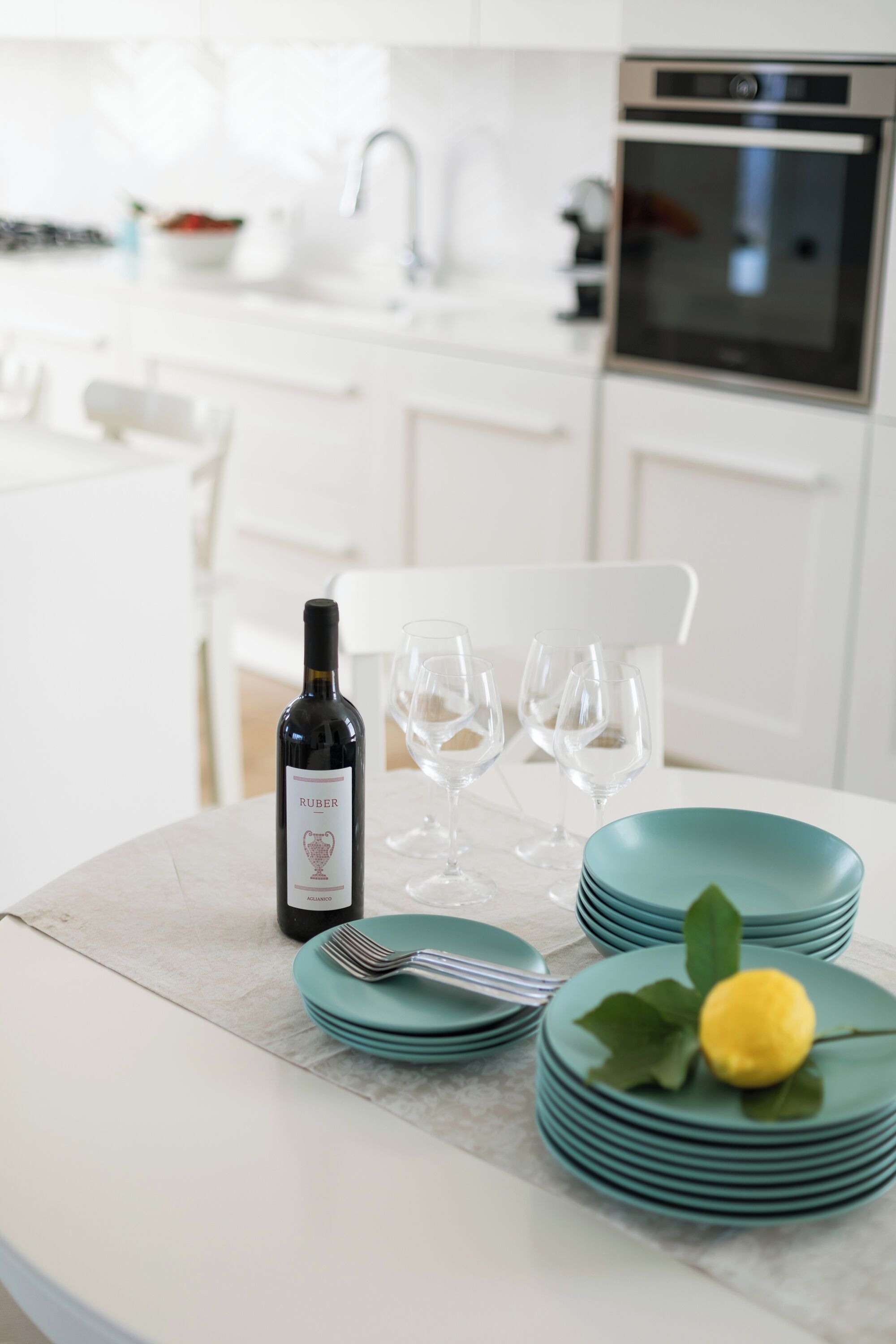 A kitchen with white cabinets, a marble countertop, a wine bottle, and teal plates.