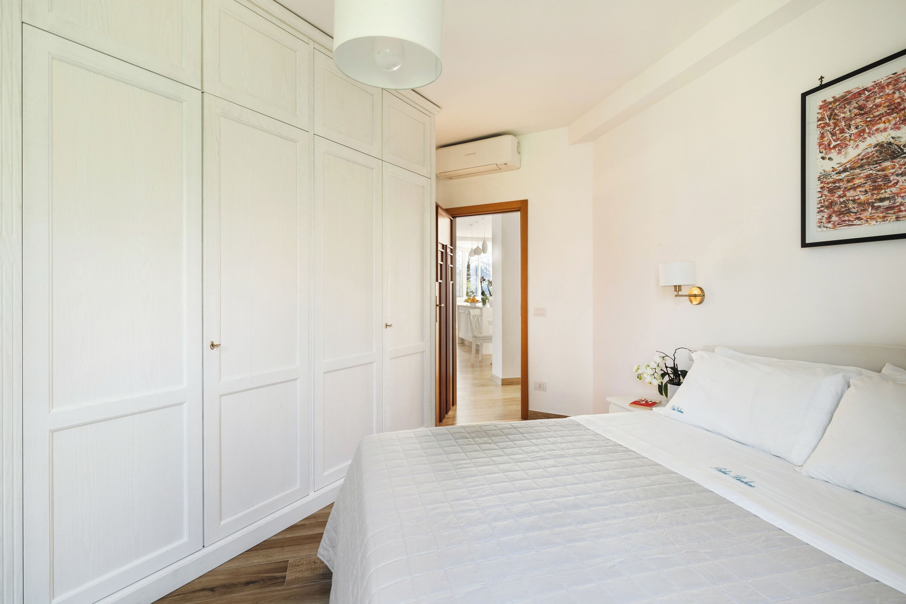 Een slaapkamer met een bed, een kledingkast, een nachtkastje en een lijst aan de muur.