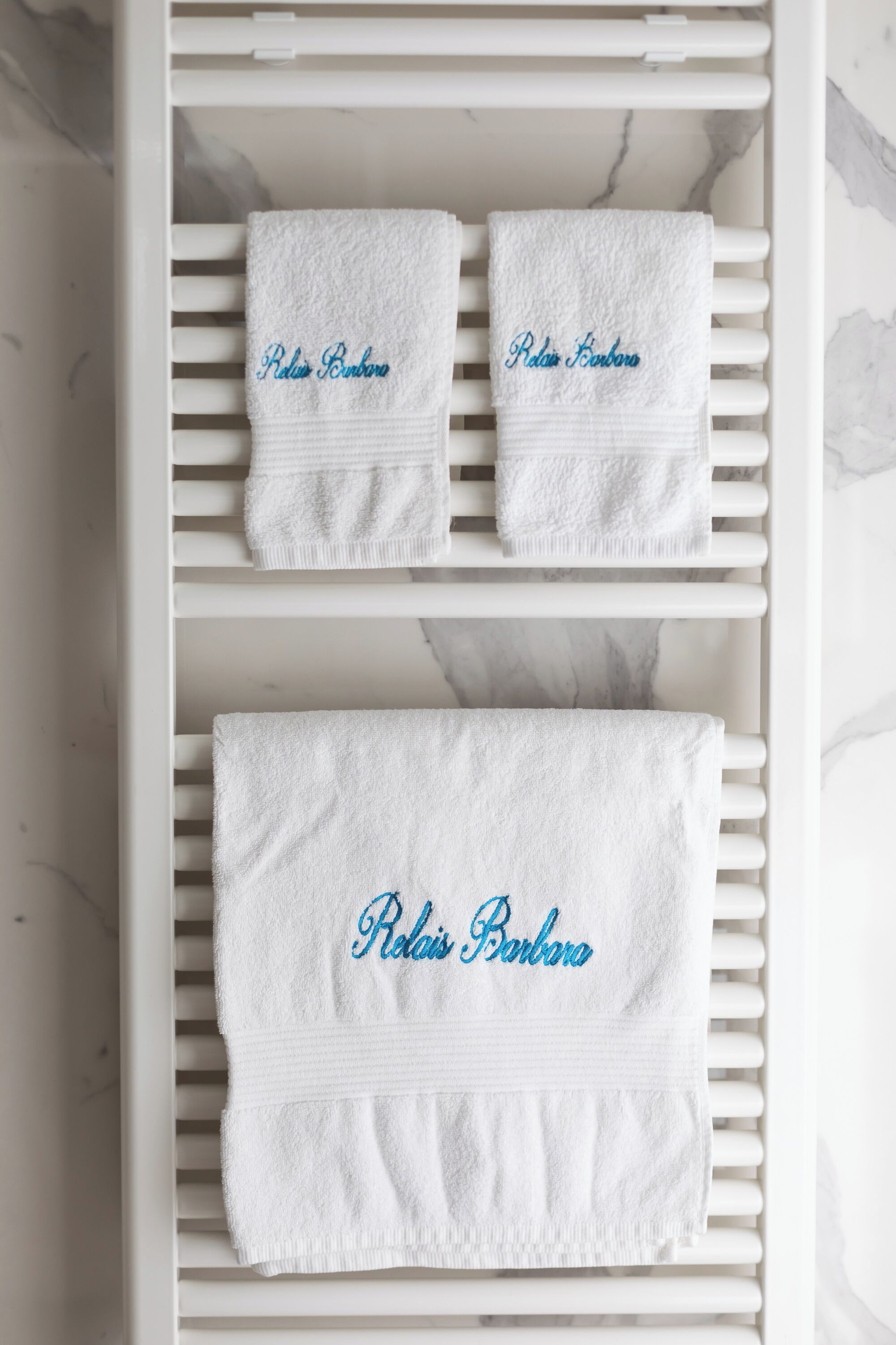 A white towel rack with three white towels, each with "Relais Barbosa" embroidered in blue.