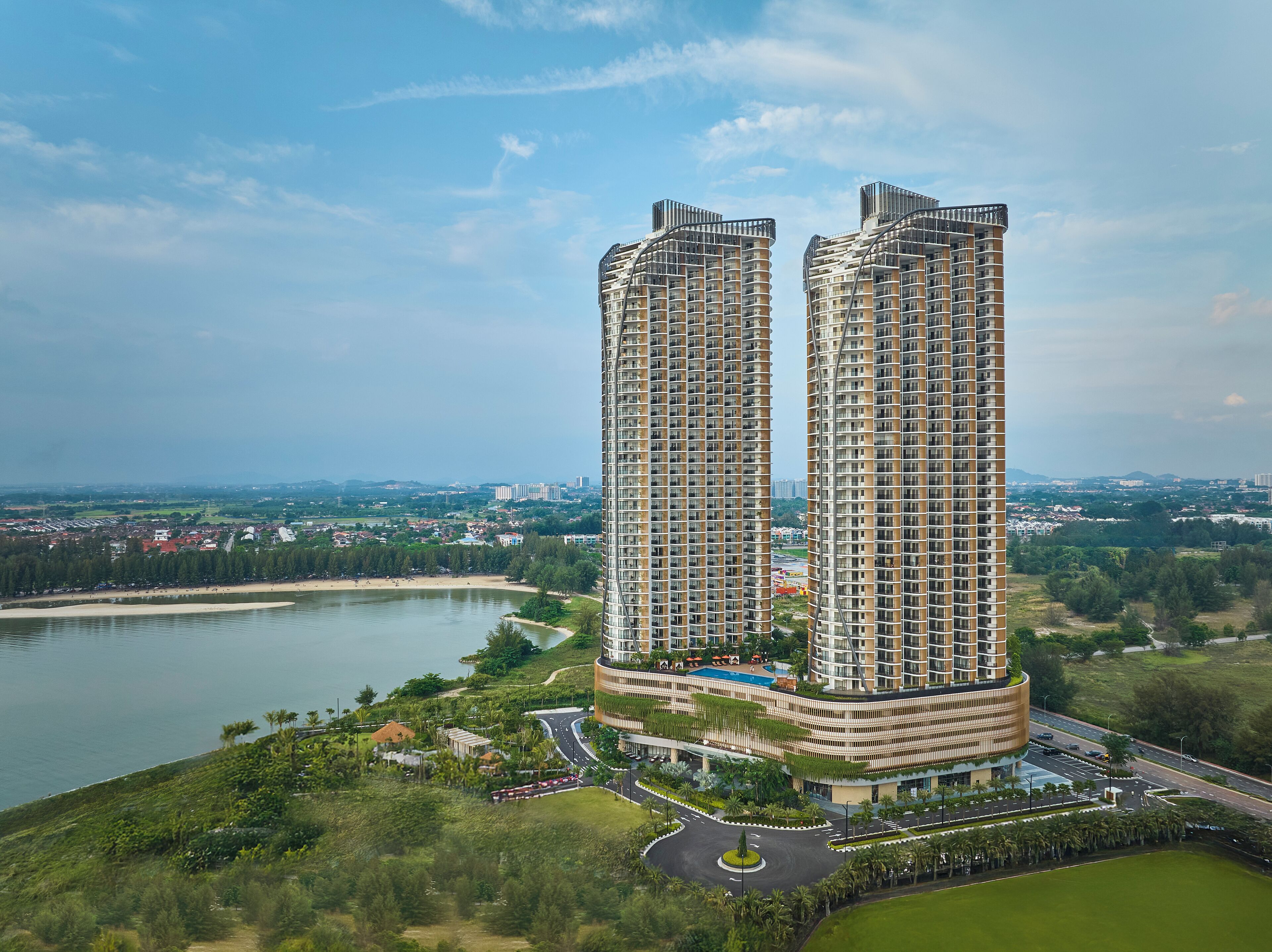 A high-rise residential building with a curved design, surrounded by greenery and a body of water.