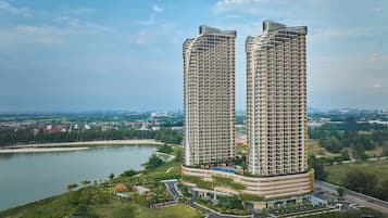 A high-rise residential building with a curved design, surrounded by greenery and a body of water.
