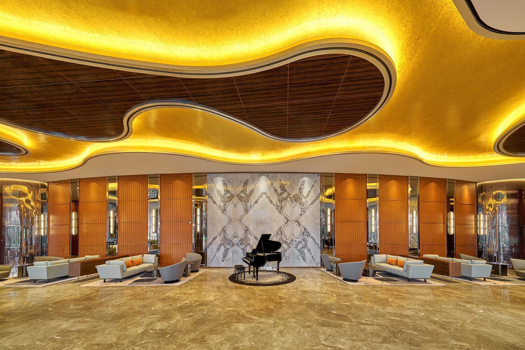 A spacious lobby with a grand piano, modern seating, and a marble wall with a unique design.