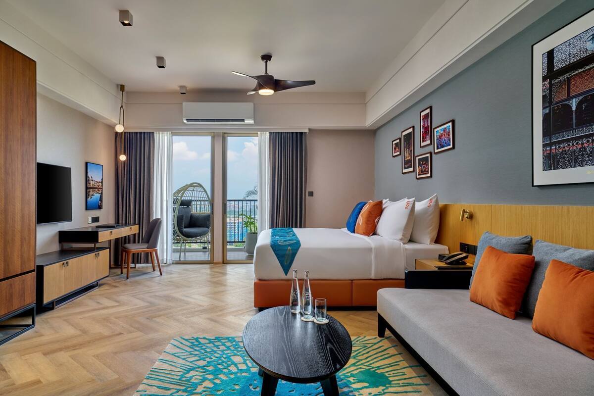 A modern hotel room with a bed, sofa, desk, and TV.