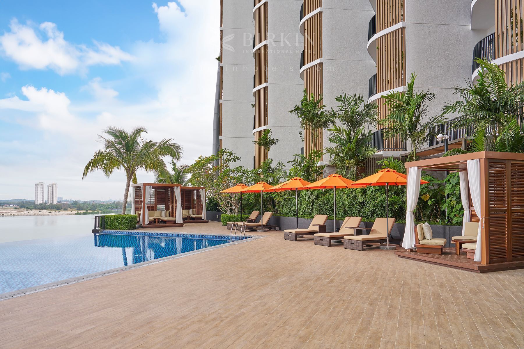 A rooftop pool area with lounge chairs and umbrellas, surrounded by tall buildings and palm trees.