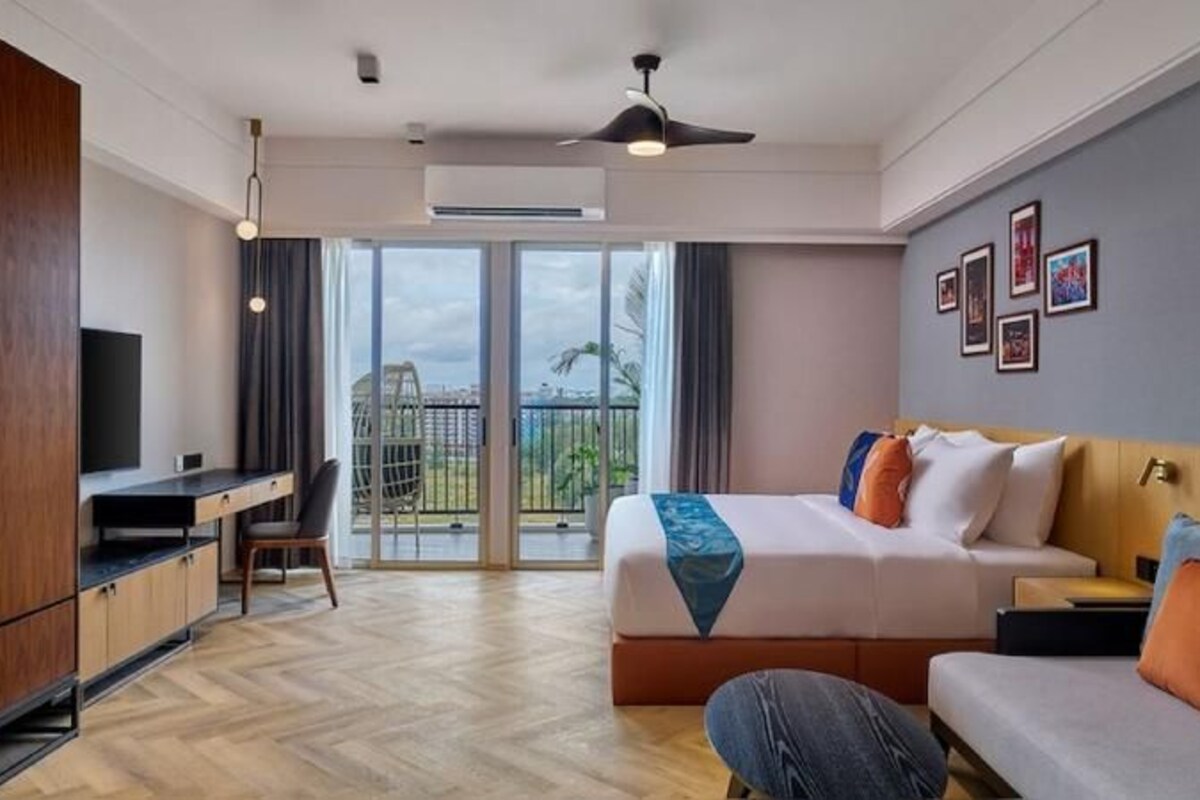 Een hotelkamer met een bed, een bureau, een bank, een balkon met uitzicht en een plafondventilator.