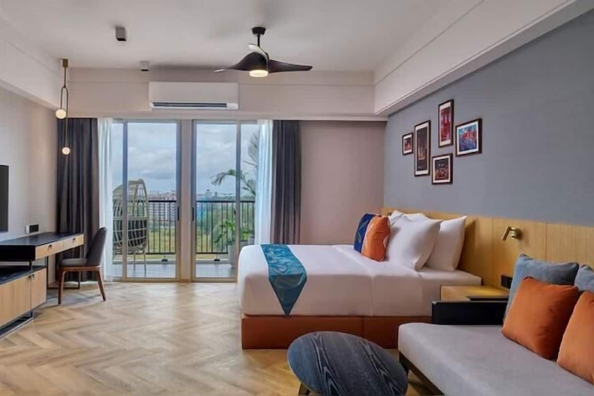 A hotel room with a bed, a desk, a sofa, a balcony with a view, and a ceiling fan.