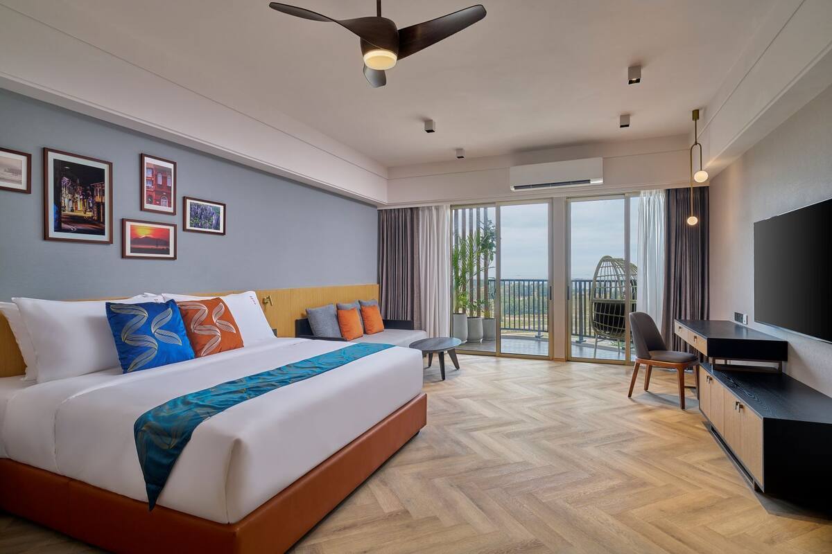 A hotel room with a large bed, a desk, a chair, a TV, and a balcony with a view.