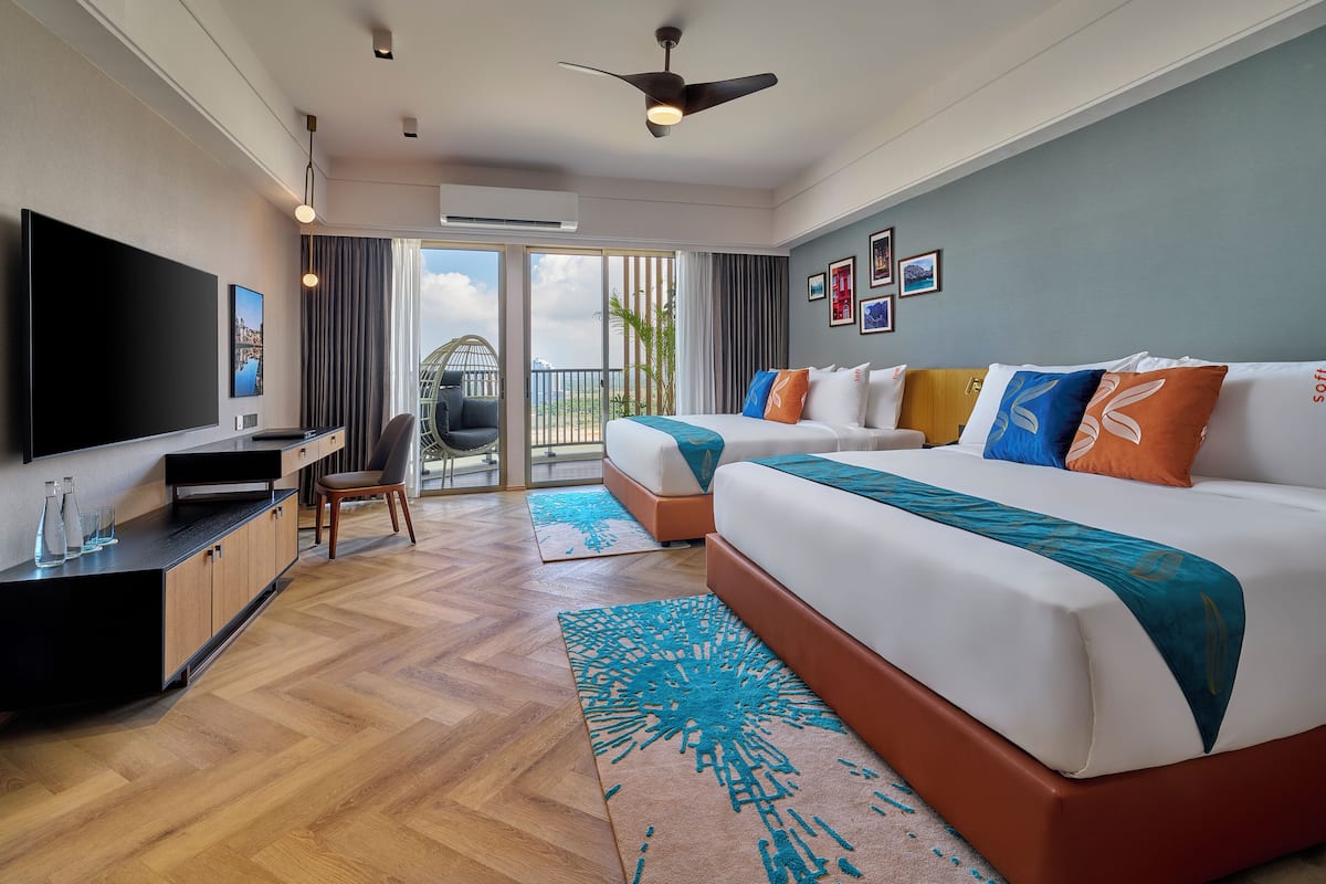 A modern hotel room with a large bed, a desk, a TV, and a balcony with a view.