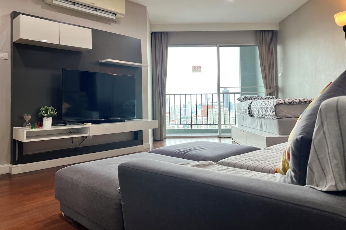 A modern living room with a flat-screen TV, a sofa, and a balcony with a city view.