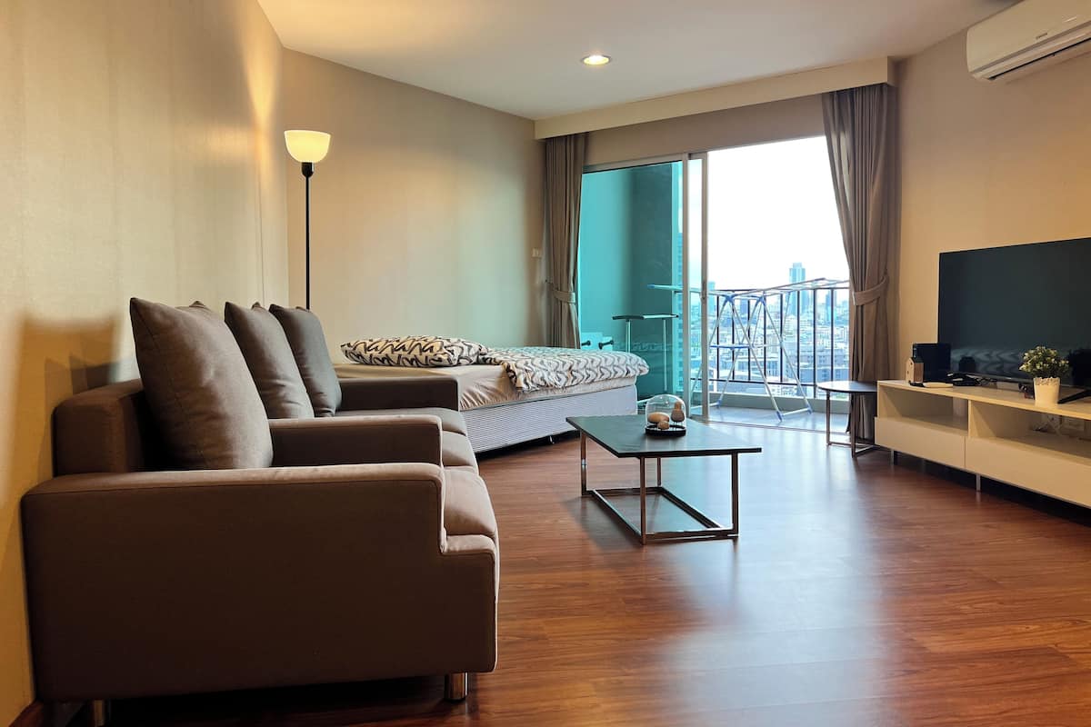A modern hotel room with a sofa, a bed, a TV, and a balcony with a city view.
