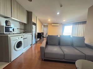 A modern apartment with a kitchen, a washing machine, a grey sofa, and a dining area. - Belle Rama9 Boutique Apartments (Bangkok)