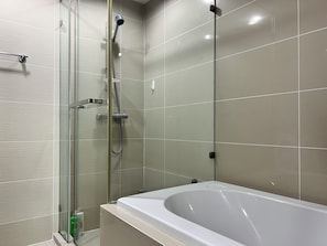 A modern bathroom with a glass-enclosed shower, a white bathtub, and tiled walls. - Belle Rama9 Boutique Apartments (Bangkok)