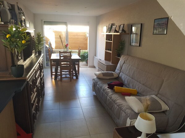A living room with a sofa, a dining table with chairs, a kitchen area, and a sliding glass door leading to a patio. - FULL APARTMENT 3 rooms 62 m2 with Balcony near TRAM T2 5 mn walk (Bezons (95870))