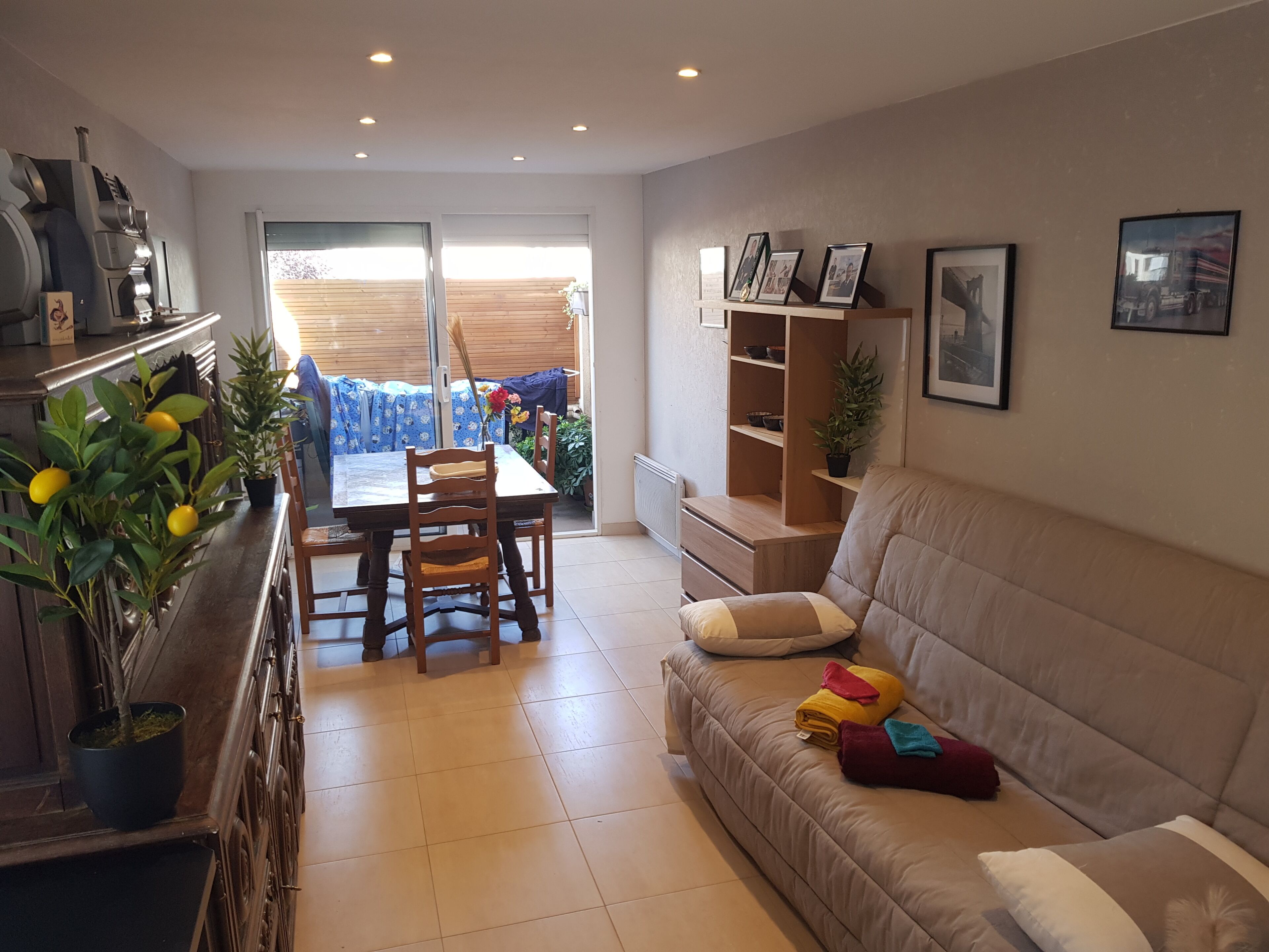 A living room with a sofa, a dining table with chairs, a kitchen area with a stove, and a sliding glass door leading to a balcony.