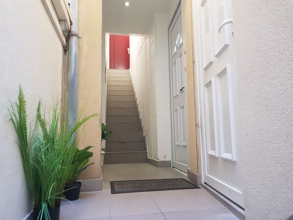 A narrow hallway with a staircase leading to a door. There are potted plants on the left side. - FULL APARTMENT 3 rooms 62 m2 with Balcony near TRAM T2 5 mn walk (Bezons (95870))