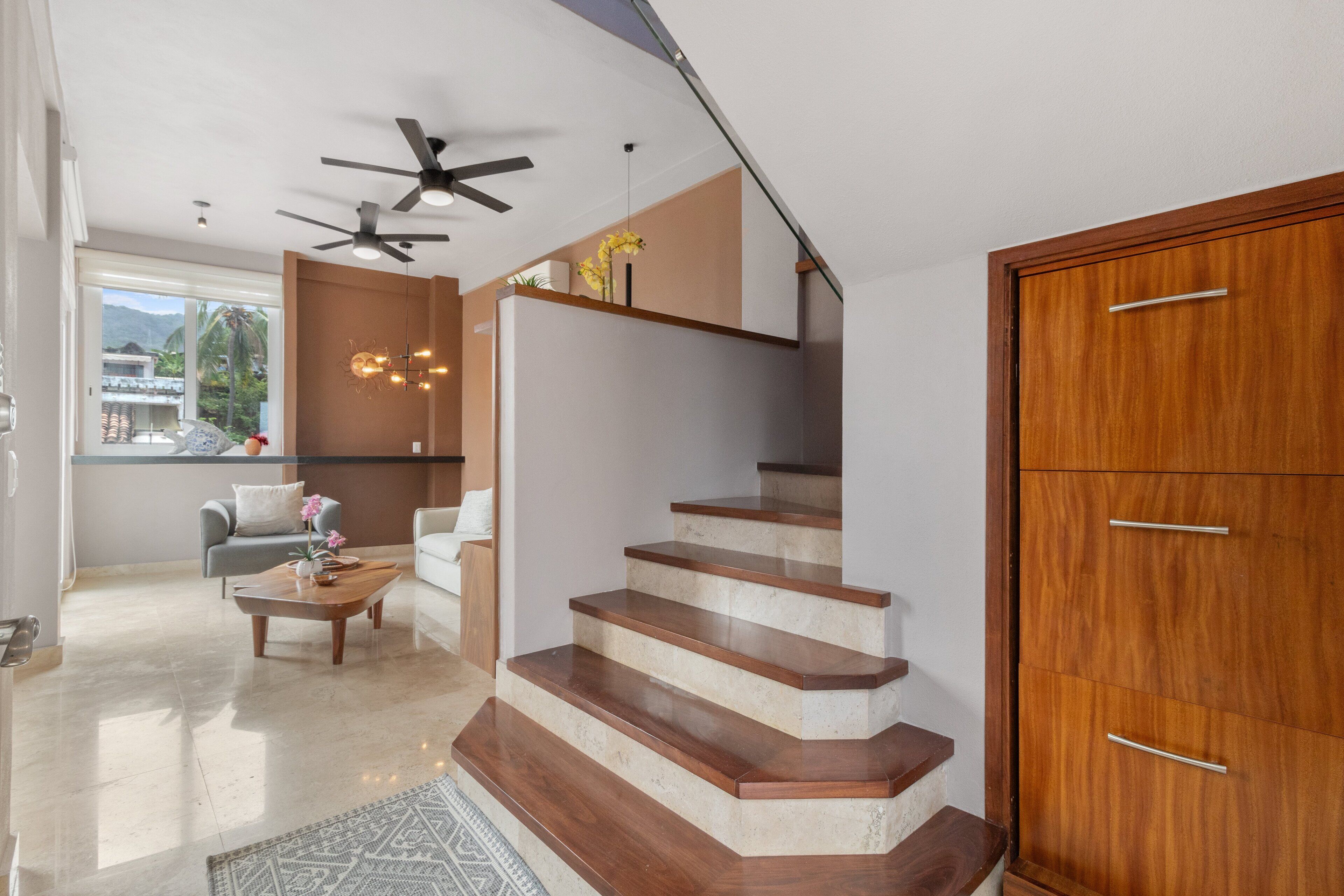 A modern interior with a wooden staircase, a ceiling fan, and a view of the outdoors.