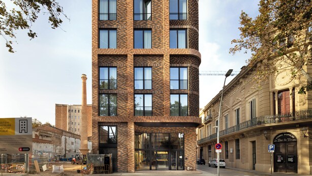 A modern multi-story building with a brick facade, large windows, and a curved corner design. - Students Studios - Student Accommodation Only (Barceelona)