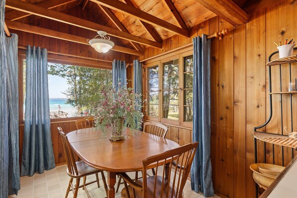Un coin repas en bois avec une table et des chaises, un vase rempli de fleurs et une vue sur la plage.