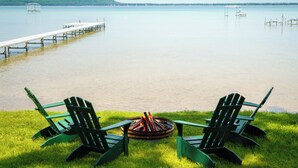 Blick auf einen See mit zwei Adirondack-Stühlen vor einem Lagerfeuer.