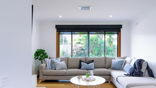 Ein modernes Wohnzimmer mit einem beigefarbenen Ecksofa, einem runden Couchtisch und einem großen Fenster mit Blick auf Grünflächen.