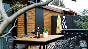 Ein Essbereich im Freien mit Holzdeck, Metallstühlen, einem Tisch und einem Grill.
