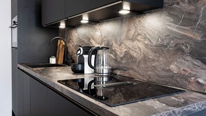 A modern kitchen with a black countertop, a stainless steel kettle, and a built-in stove.