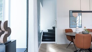 A modern interior with a staircase, a dining area with orange chairs, and a minimalist decor.