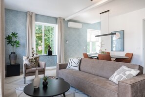 A modern living room with a sofa, armchair, and coffee table, a dining area with chairs and a table, and large windows with curtains. - 2 Bedroom Apartment with 4 Beds and a chairbed - Perfect for groups! (Nijmegen)