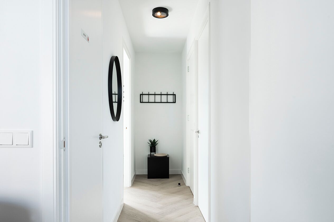 Un couloir aux murs blancs, orné d’un motif circulaire noir, avec un objet rectangulaire noir et une petite plante posée sur un socle noir.