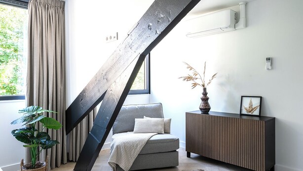 A modern living room with a grey sofa, a wooden cabinet, a large window with curtains, and a potted plant.