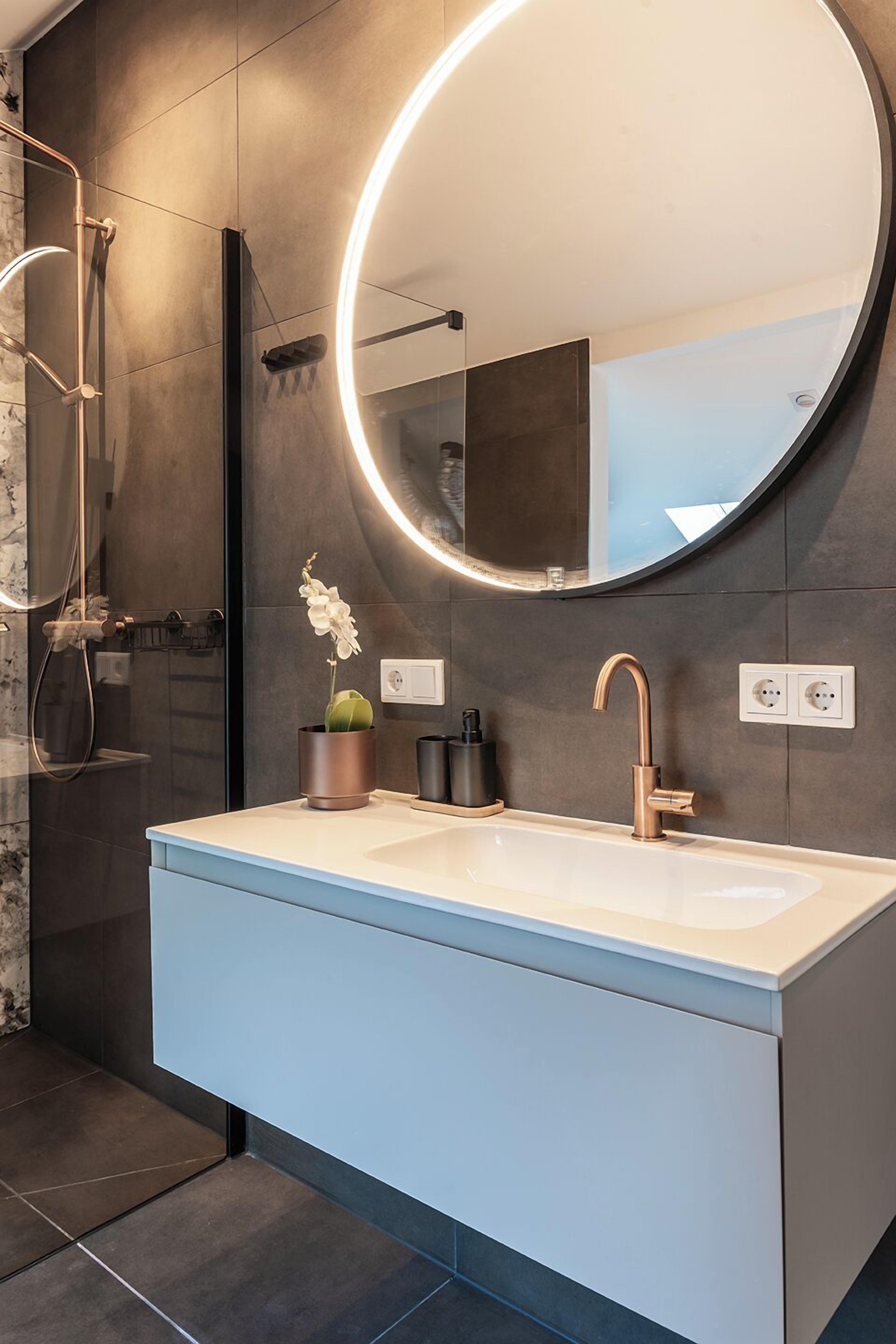 A modern bathroom with a large mirror, a sink, and a shower.