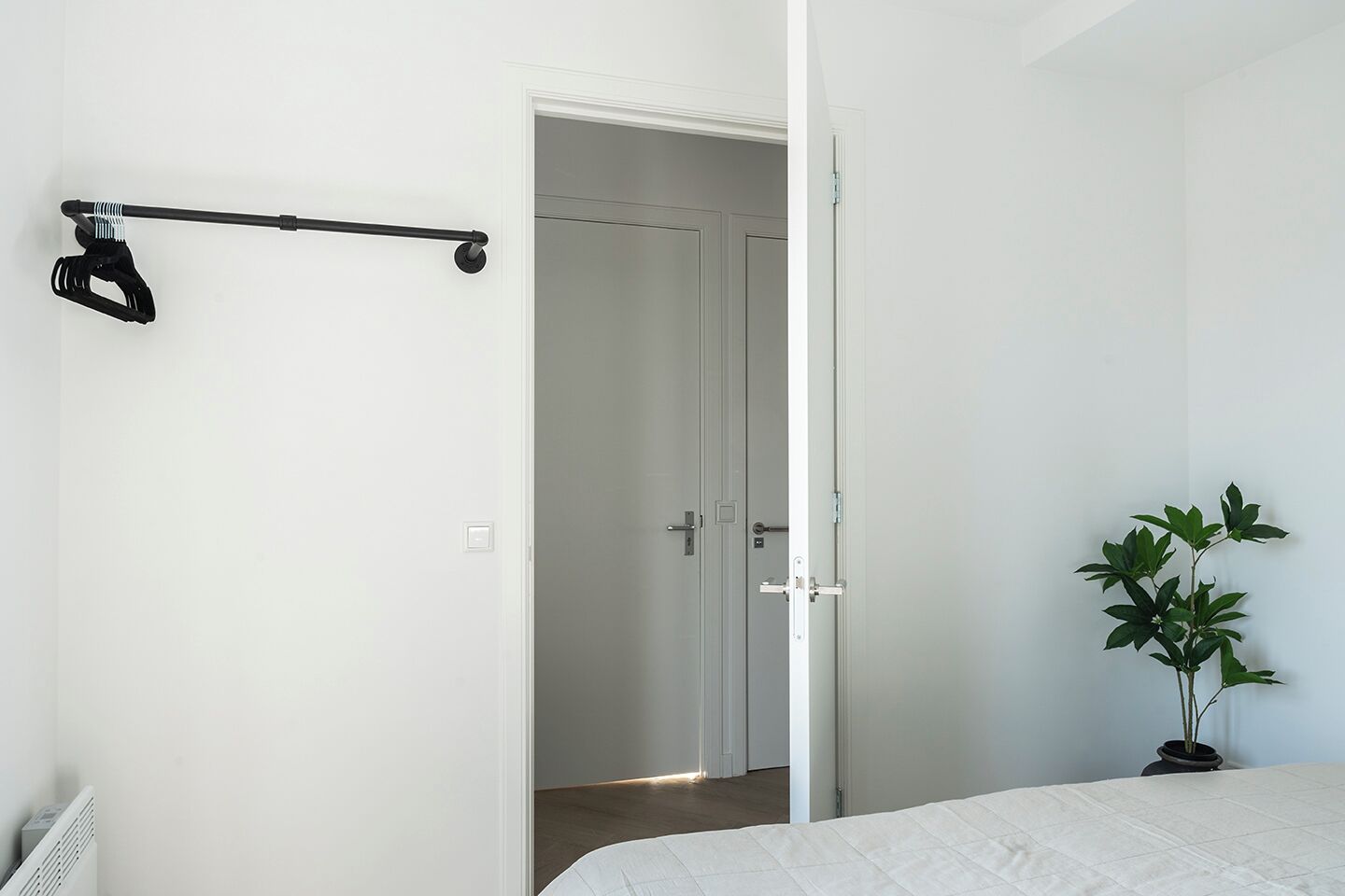 Une chambre à coucher avec un lit, une porte donnant sur une autre pièce, un radiateur et une plante en pot.