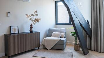 Een moderne woonkamer met een grijze bank, een houten console tafel, een groot raam en een opvallende zwarte metalen trap.