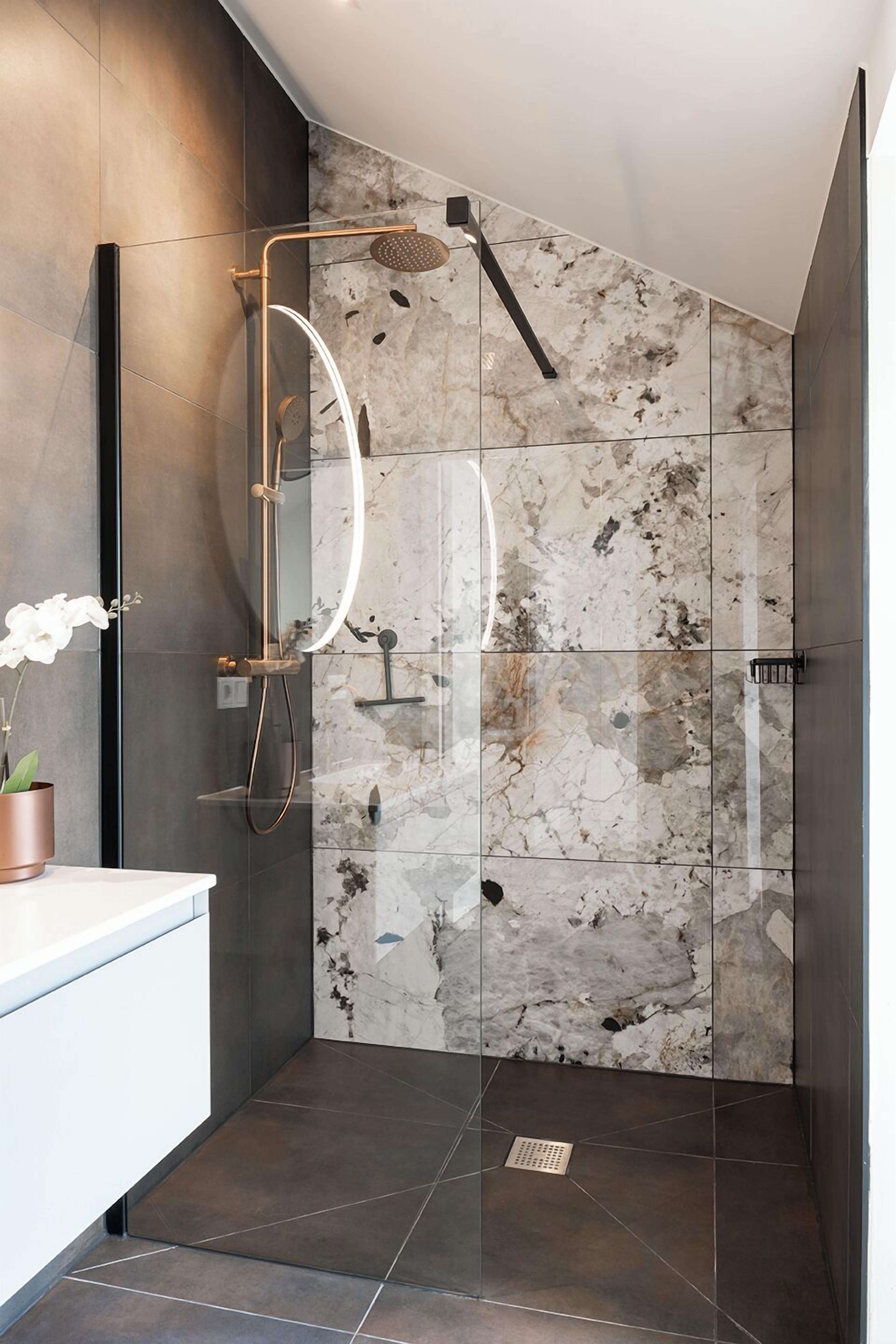 Une salle de bain moderne dotée d’une douche à parois de verre, de carreaux de marbre et d’un design minimaliste.