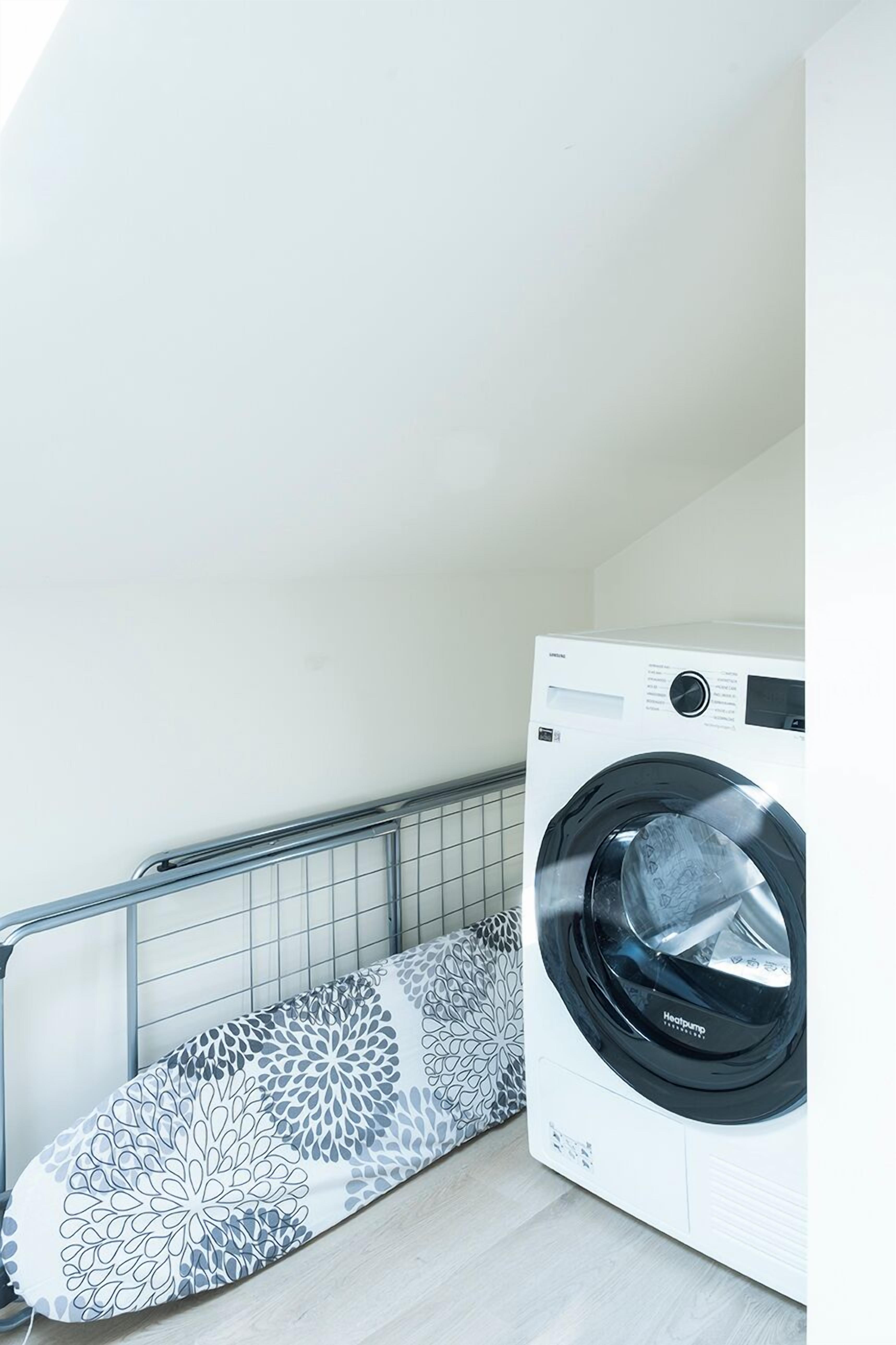A compact laundry room with a front-loading washing machine and a patterned ironing board.