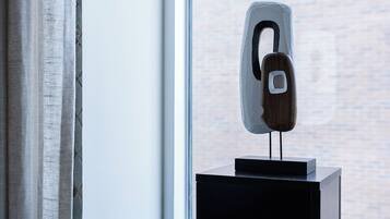 Une sculpture moderne, posée sur un piédestal près d’une fenêtre, avec un mur de briques en arrière-plan.