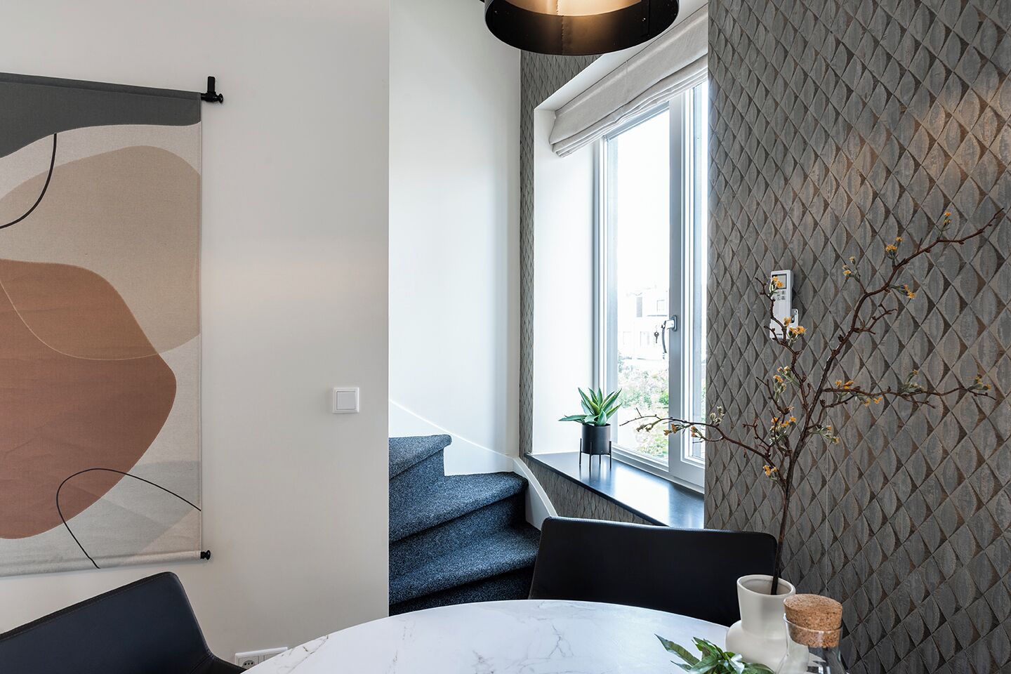 A modern dining area with a round table, dark chairs, a potted plant, and a window with a view.