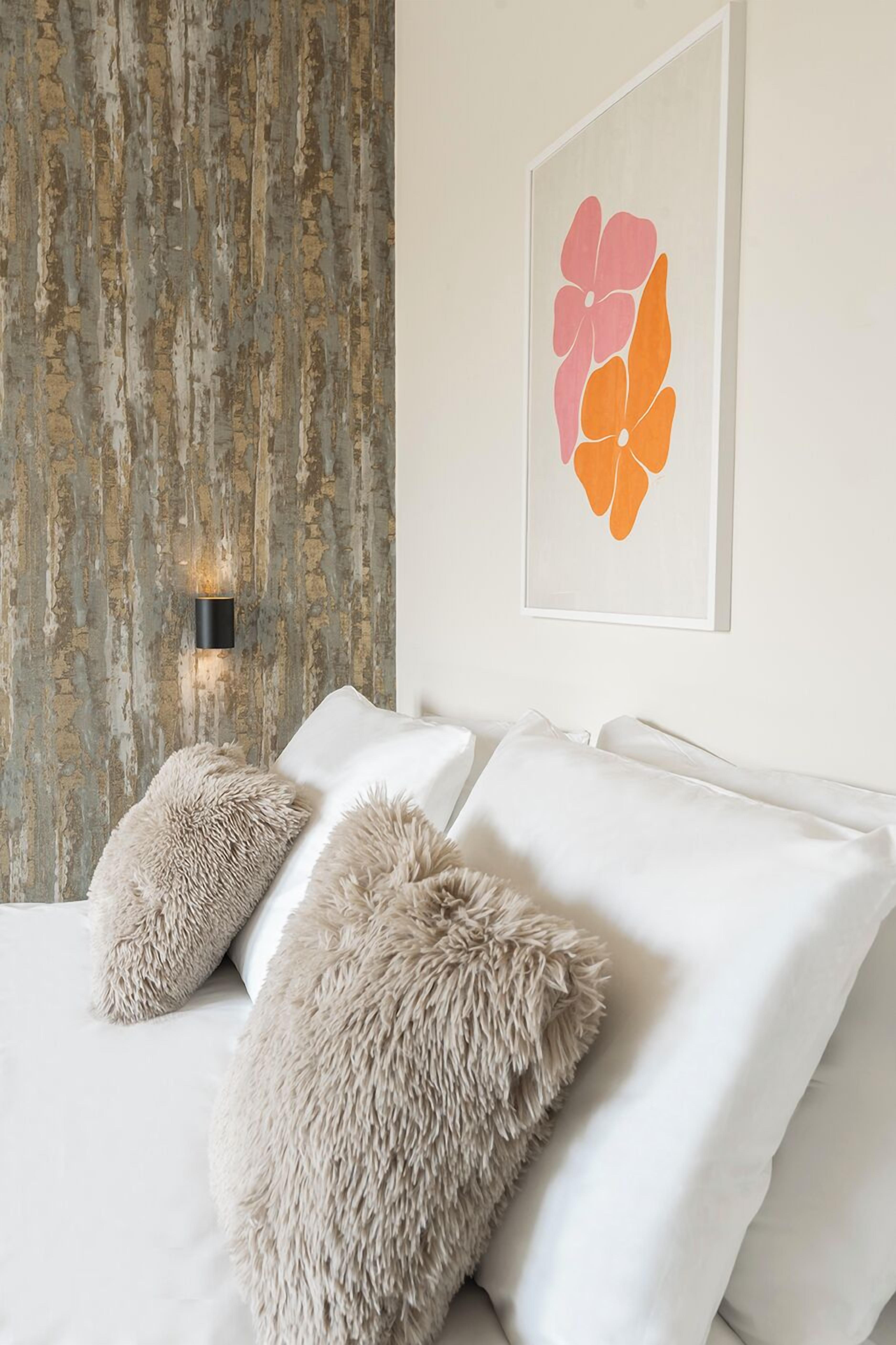 Un dormitorio con pared rústica, una obra de arte abstracta enmarco y una cama con almohadas mullidas.