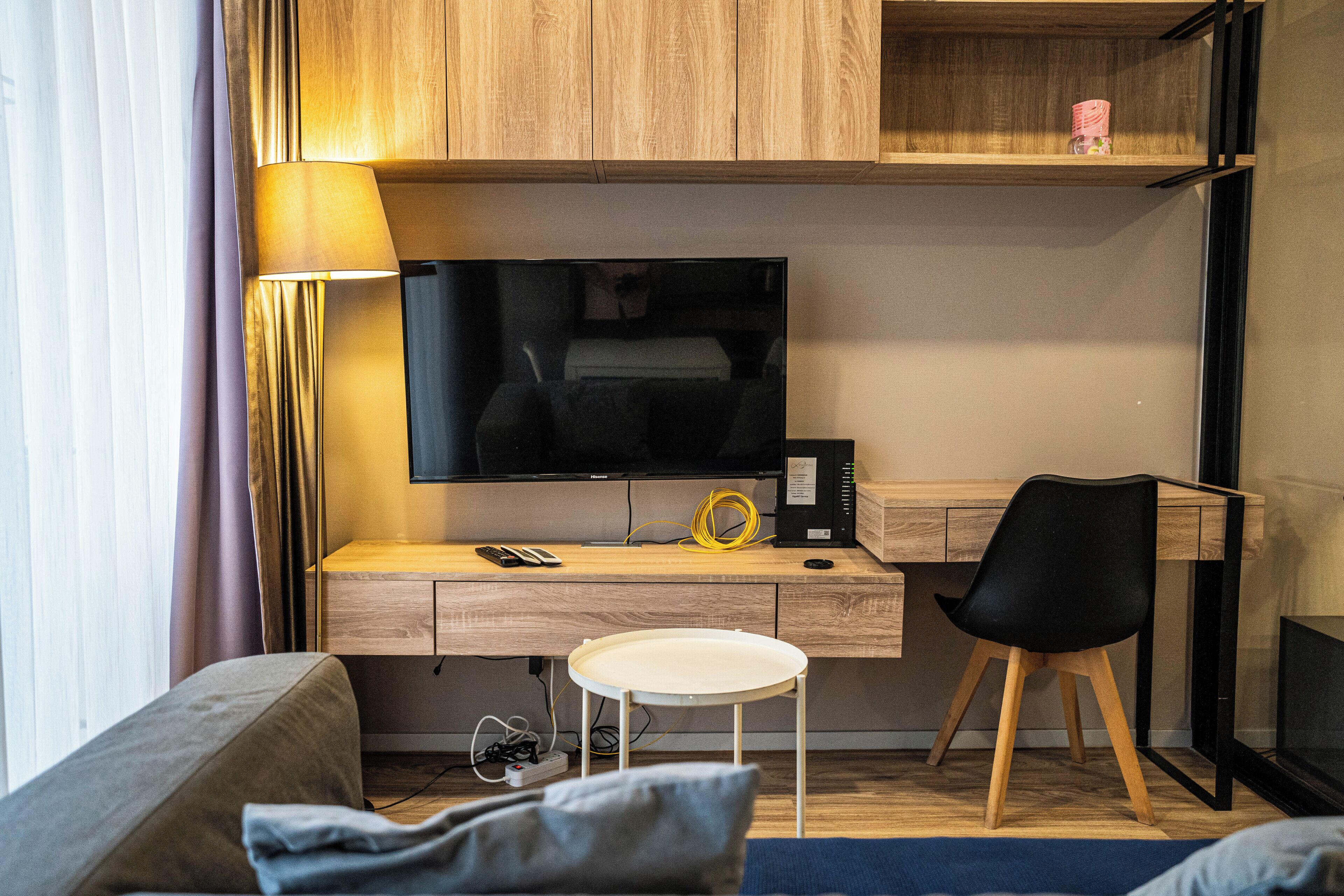 A modern room with a wooden desk, a flat-screen TV, a black chair, and a small table.
