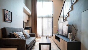 A modern living room with a sofa, coffee table, TV, and a staircase leading to an upper level.