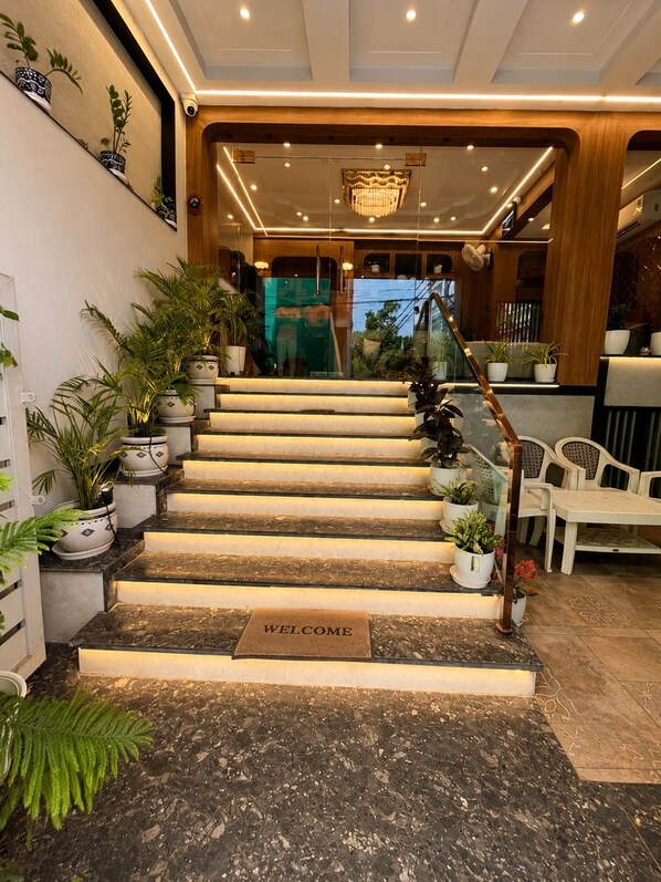 A staircase with a welcome mat at the bottom, leading to a reception area with a chandelier and potted plants. - Hotel Om Villa (Varanasi)