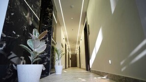 A modern hotel hallway with marble walls, potted plants, and recessed lighting. - Hotel Om Villa (Varanasi)