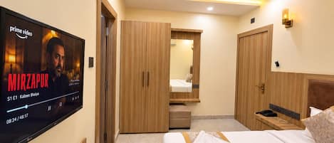 A hotel room with a flat-screen TV, wooden wardrobe, a bed with a marble-patterned bedspread, and a ceiling fan.