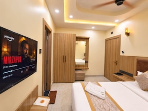 A hotel room with a flat-screen TV, wooden wardrobe, a bed with a marble-patterned bedspread, and a ceiling fan. - Hotel Om Villa (Varanasi)