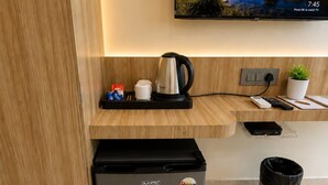 A modern kitchenette with a coffee maker, a small fridge, a trash bin, and a TV displaying a scenic landscape. - Hotel Om Villa (Varanasi)